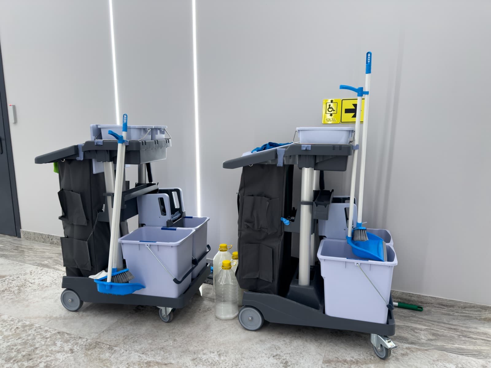 Two janitorial carts with buckets, mops and brooms ready in a facility hallway