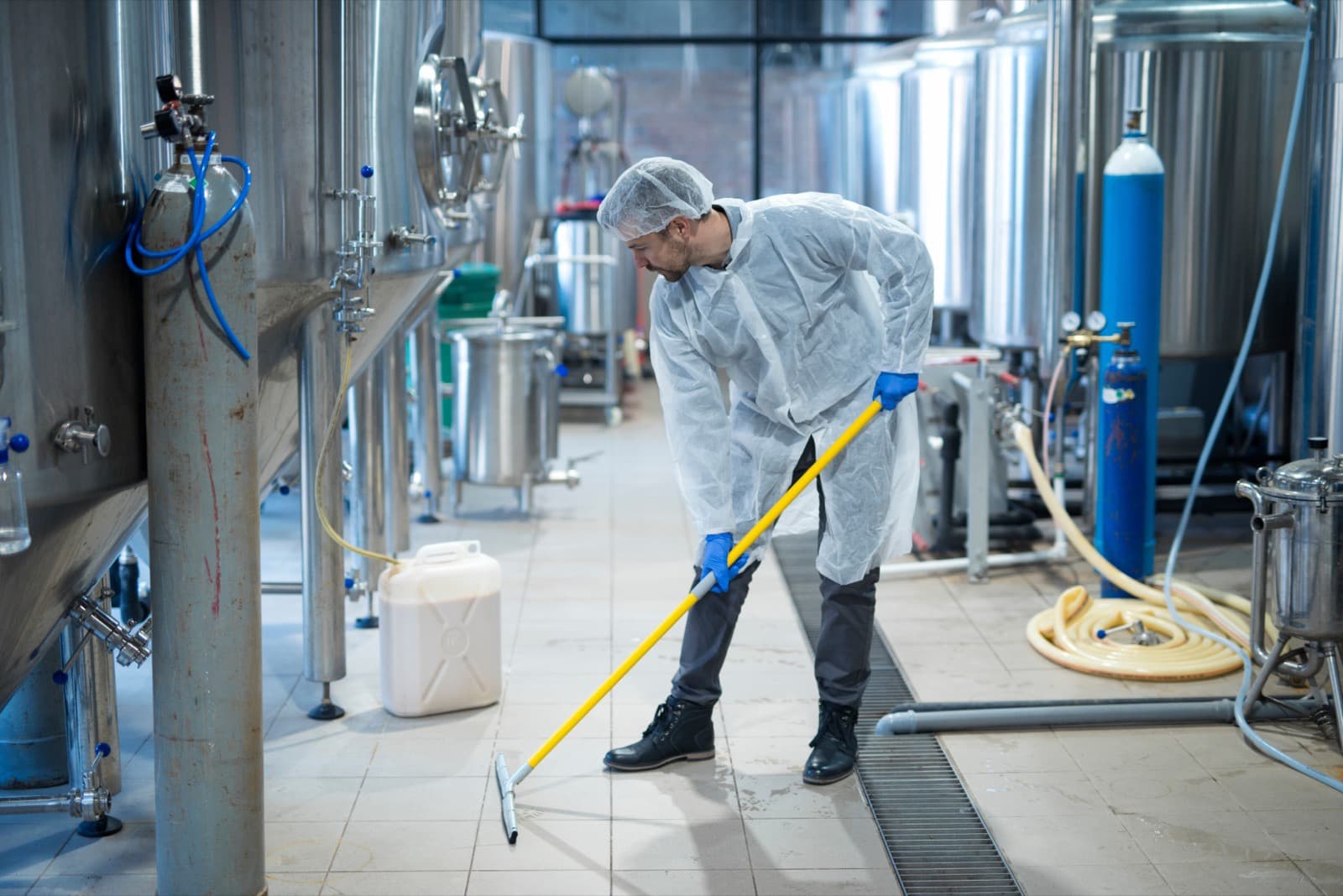 Worker in protective clothing cleaning a production area floor